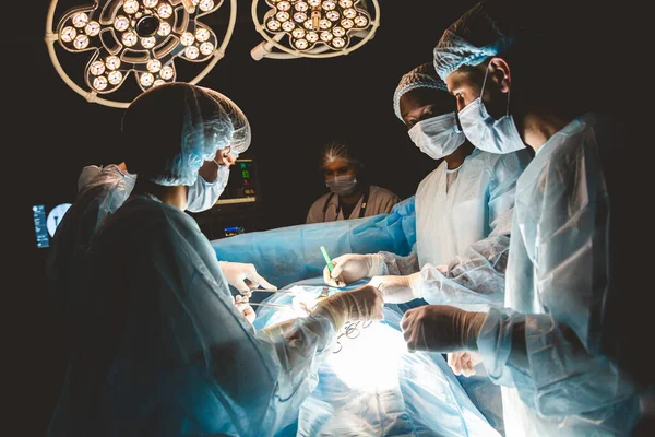 Une équipe internationale de médecins effectue une opération chirurgicale complexe sur un patient sous anesthésie. Une salle d'opération moderne et des chirurgiens expérimentés sauvent des vies — Photo