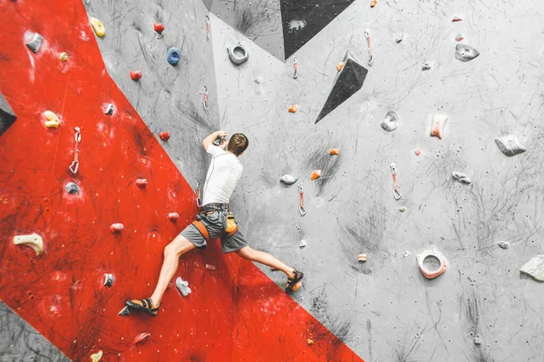 Спортсмен поднимается по крутой скале, взбирается на искусственную стену в помещении. Экстремальные виды спорта и боулдеринг — стоковое фото
