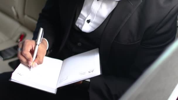 Homem de negócios indiano elegante faz anotações em um caderno enquanto está sentado em um carro. — Vídeo de Stock