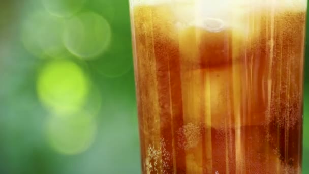 Close-up van een glas met een verfrissend koud drankje met stukjes ijs en borrelende vloeistof op een wazig zomerbladerdek — Stockvideo