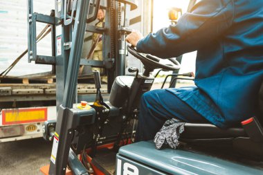 Forklift kullanan bir adam büyük bir depoda çalışır ve bir çanta dolusu hammaddeyi boşaltır.