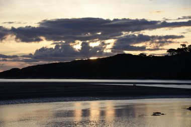 Küçük dalgalar ile gün batımında Raglan beach