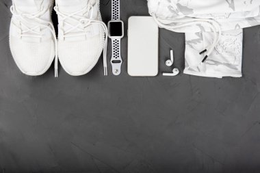 Formda ve sağlıklı yaşam tarzı konsepti. Şık fitness aksesuarları: spor ayakkabıları, kamuflaj eğitim kapüşonu, akıllı telefon, akıllı saat, koyu gri beton arka planda kablosuz kulaklık. Düz yat, boşluğu kopyala.