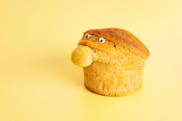 Homemade muffin with a big nose and small eyes on a yellow background. Funny food character.