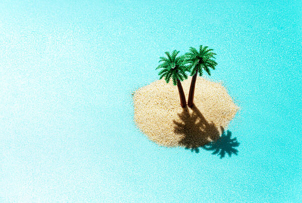 Miniature toy tropical island with palm trees in the ocean. Harsh sunlight effect, copy space. Creative summer vacation concept.