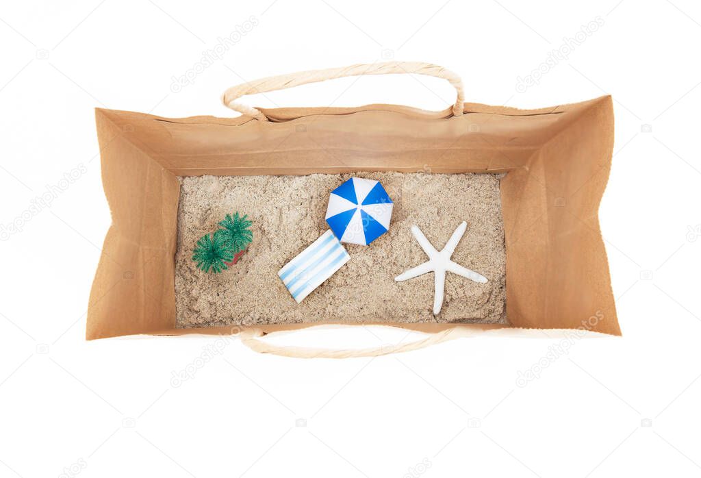 Miniature toy beach with a lounge chair, palm trees, sun umbrella and a white starfish inside a paper shopping bag. Booking summer vacation packages concept.