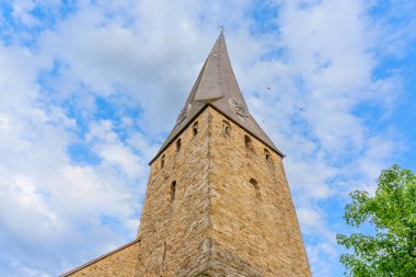 Dinamik bir gökyüzünün altında, yemyeşil bulutlarla dolu tarihi bir kilisenin uzun taş kulesi..