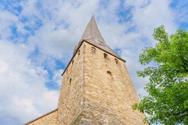 Belirgin bir saate sahip taştan bir kilise kulesinin alçak açılı görüntüsü bulutlu bir gökyüzüne doğru yükseliyor mimari detayları ve tarihsel önemi vurguluyor..