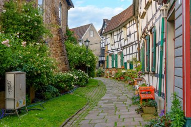 Hattingen, Almanya - 14 Haziran 2025: Hattingen, Almanya 'da yarım ahşap evler, çiçek açan çiçekler ve klasik sokak lambaları ile kaplı Picturesque kaldırım taşı geçidi.