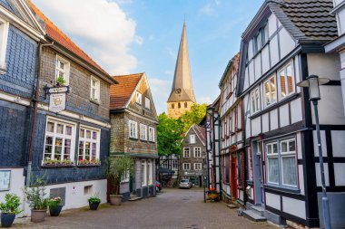 Hattingen, Almanya - 14 Haziran 2025: Hattingen, Almanya 'da tarihi sokaklar, geleneksel ahşap çerçeveli evler ve hareketli bir ufuk çizgisine karşı yüksek bir kilise kulesi.