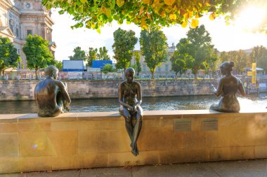 Berlin, Almanya - 17 Ağustos 2025: Berlin 'de gün batımında nehir kenarında oturan üç heykelin bronz heykelleri.