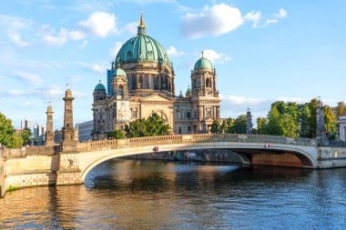 Berlin, Almanya - 17 Ağustos 2025: Berlindeki yemyeşil katedralin manzarası, taştan bir köprü ve açık gökyüzünün altındaki Spree Nehri.