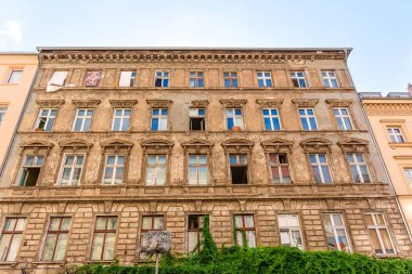 Berlin, Almanya - 17 Ağustos 2025: Berlin 'deki yıpranmış bir binanın ayrıntılı görüntüsü, açık mavi gökyüzüne karşı süslü pencere çerçeveleri ve kırsal bir estetik içeriyor.