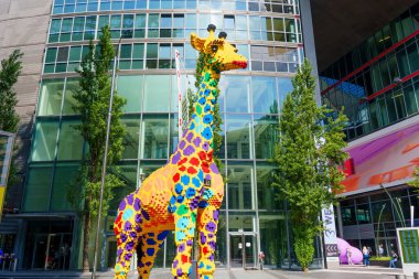 Berlin, Almanya - 16 Ağustos 2025: Berlin 'deki modern cam binanın önünde duran plastik tuğlalardan yapılmış canlı zürafa heykeli.