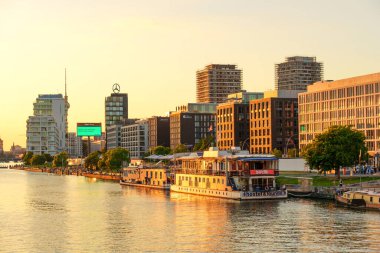 Berlin, Almanya - 18 Ağustos 2025: Çağdaş binalar ve bir teknenin yer aldığı Spree Nehri 'nin günbatımında manzarası.