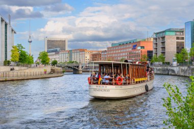 Berlin, Almanya - 20 Ağustos 2025: Berlin 'deki Spree Nehri boyunca turistler ve arka planda TV Kulesi ile birlikte renkli tekne gezisi.
