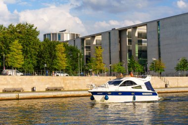 Berlin, Almanya - 20 Ağustos 2025 Berlin 'deki çağdaş bir parlamento binasının önündeki nehir boyunca uzanan tekne, berrak mavi gökyüzünün altındaki yemyeşil ağaçlarla çevrilidir..