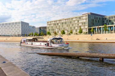 Berlin, Almanya - 20 Ağustos 2025: Berlin 'deki bir su yolunda yüzen Carola adında bir tekne, parçalı bulutlu bir gökyüzü altında çağdaş binalarla çevrili..