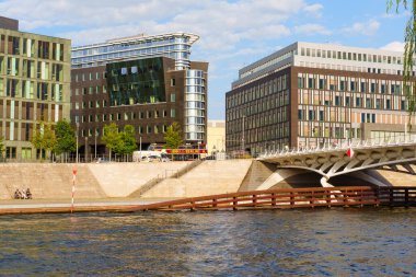 Berlin, Almanya - 20 Ağustos 2025: Berlin 'deki Spree Nehri' nin yanındaki çağdaş binaların çarpıcı görüntüsü, modern tasarım unsurları, yemyeşil alanlar ve limanın tadını çıkaran ziyaretçiler sergileniyor.