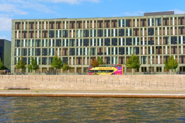 Berlin, Almanya - 20 Ağustos 2025: Berlin 'de Federal Eğitim ve Araştırma Bakanlığı' nın çağdaş yapı cephesi, geniş pencereler, yeşillikler ve nehir kıyısının yanında bir tur otobüsü yer alıyor..