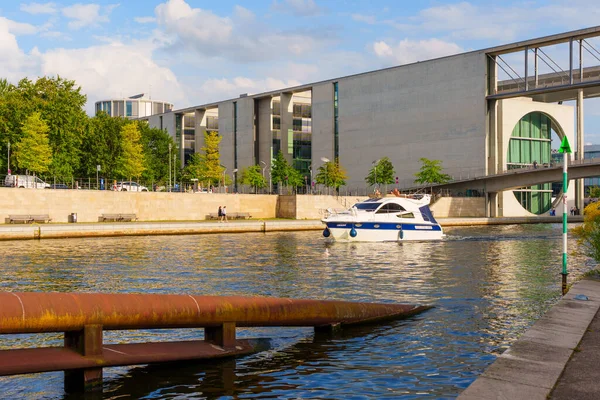 Berlin, Almanya - 20 Ağustos 2025: Çağdaş federal binalar Berlin 'deki nehir kıyısında, yeşillik ve denizde yüzen bir tekne ile kentsel mimari ve doğanın bir karışımını yakalıyorlar..