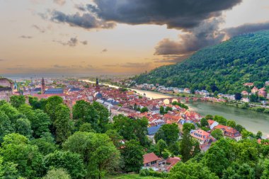 Almanya, Heidelberg 'in panoramik manzarası, Neckar Nehri, tarihi binalar, yemyeşil ve gün batımında dramatik bulutlar.