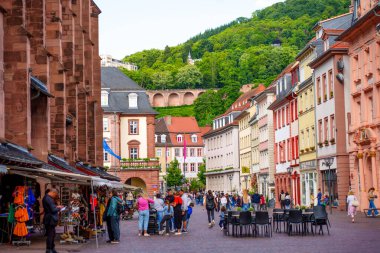 Heidelberg, Almanya - 8 Haziran 2025: Heidelberg 'de canlı yayalar, arka planda tarihi mimari, canlı turistler ve yemyeşil tepeler sergileniyor.
