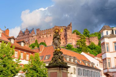 Heidelberg, Almanya - 8 Haziran 2025: Kornmarkt 'taki Madonna çeşmesinin heykeli, tarihi binalar ve dramatik gökyüzünün altındaki Heidelberg Kalesi tarafından çerçevelendi.