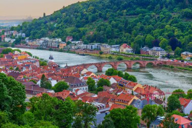 Heidelberg, Almanya - 8 Haziran 2025: Heidelberg 'in canlı eski kasabasını, yemyeşil tepeleri ve Neckar Nehri üzerindeki ikonik eski köprüyü altın saat boyunca görüntüleyen panoramik manzara.