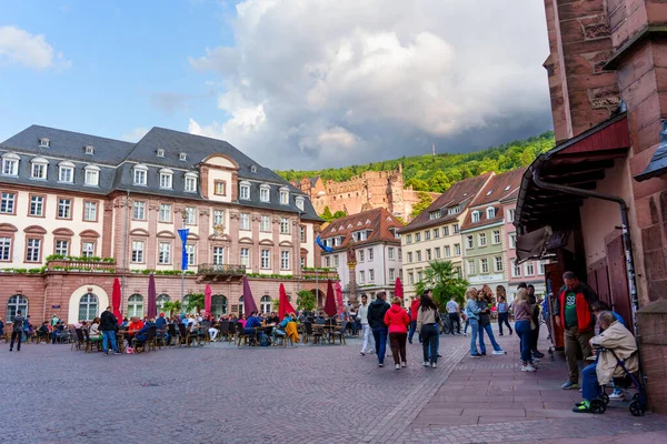 Heidelberg, Almanya - 8 Haziran 2025: Heidelberg Meydanı 'nda tarihi mimari, açık hava kafeleri ve dramatik bulutlar altındaki hareketli atmosferin keyfini çıkaran ziyaretçiler.