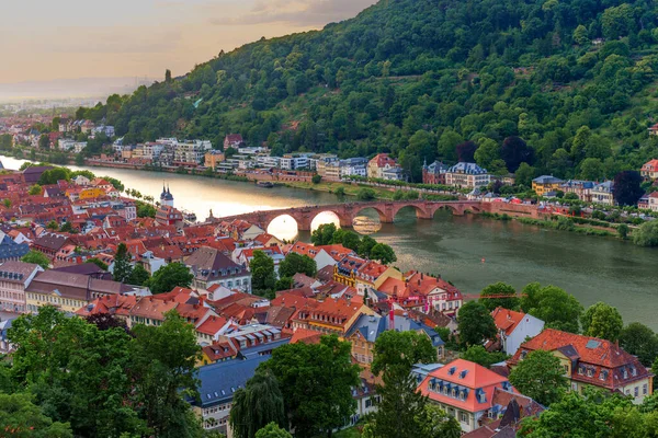 Heidelberg, Almanya - 8 Haziran 2025: Heidelberg 'in pitoresk eski şehri Neckar Nehri' nin panoramik manzarası ve günbatımındaki ikonik köprü, yemyeşil tepeler ve renkli çatılarla çevrili.