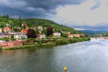 Heidelberg, Almanya - 8 Haziran 2025: Renkli binalar, yemyeşil tepeler ve dramatik bir gökyüzü içeren Heidelberg manzarası.