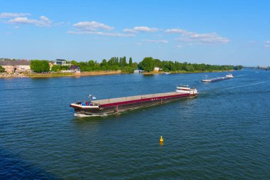 Mainz, Almanya - 19 Haziran 2025: Kargo gemileri Ren Nehri 'nin sakin sularında berrak mavi bir gökyüzü altında geçerek Mainz manzarasını gözler önüne seriyor..