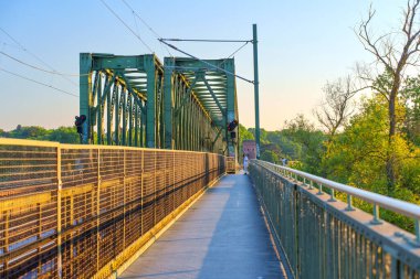 Mainz, Almanya - 19 Haziran 2025: Gün batımında Mainz, Almanya 'da yeşil bir köprüde yürüyüş, ağaçlar ve açık hava ortamında sinyal lambaları.