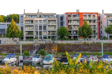 Mainz, Almanya - 19 Haziran 2025: Canlı bir gün batımına karşı teknelerle dolu bir marinaya bakan balkonların yer aldığı modern konut binaları rıhtımda yer alıyor..