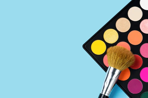 Parlak renkli sarı, kırmızı, pembe, turuncu göz farı ve pastel mavi arka plan köşesinde düzenlenmiş palet üzerine döşeme bir büyük makyaj fırça siyah plastik palet studio ile yukarıdan ışık vurdu