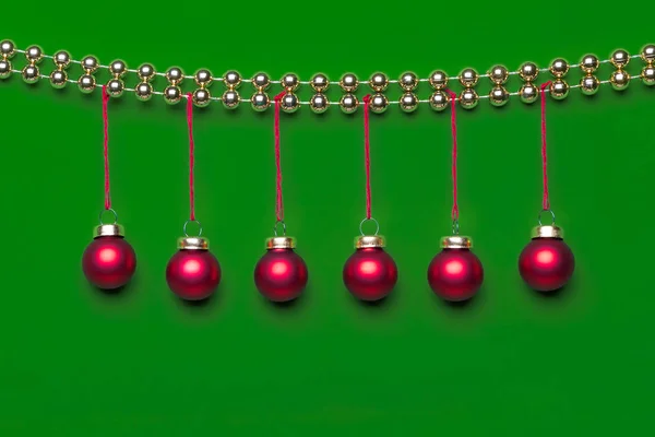 Asılı altı küçük mat kırmızı renkli Noel süsler bir satır parlak altın renginde Noel boncuk çelenk stüdyo ışık yeşil zemin üzerine tarafından dekore edilmiş