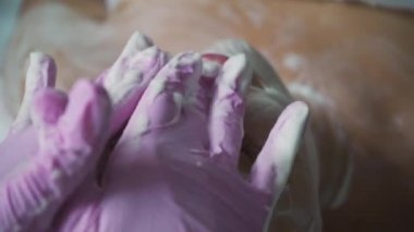 Pembe eldivenli güzellik, kızın yüzünü, omuzlarını ve dcolletini yıkar. Masaj dan önce spa salonunda cilt temizliği.