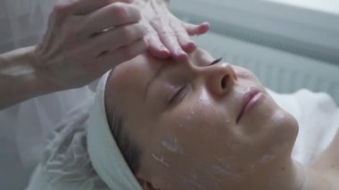 Güzellik salonunda kozmetik tedavisi gören bir kadın. Kozmetik uzmanı tıp eldivenleri kızın yüzüne dokunuyor. Profesyonel masajla yüz temizleme. Vücut ve cilt bakımı, sağlık, refah..