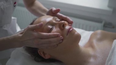 Güzellik salonunda kozmetik tedavisi gören bir kadın. Kozmetik uzmanı tıp eldivenleri kızın yüzüne dokunuyor. Profesyonel masajla yüz temizleme. Vücut ve cilt bakımı, sağlık, refah..
