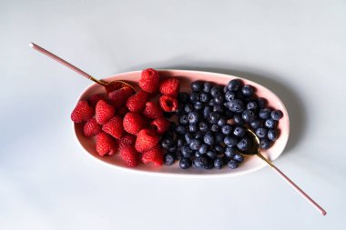 Yaz meyveleri yaban mersini, çay kaşığı ile pembe renk yeni zarif tabaklarda ahududu. İzole beyaz arka plan üzerinde yukarıdan yeni lüks Altın çatal görünümü. Üstte görüntü.