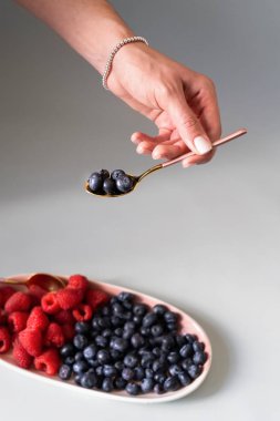 Yaz meyveleri yaban mersini, ahududu pembe renk yeni zarif tabaklar bir çay kaşığı tutan bir el ile. İzole beyaz arka plan üzerinde yukarıdan yeni lüks Altın çatal görünümü. Üstte görüntü.