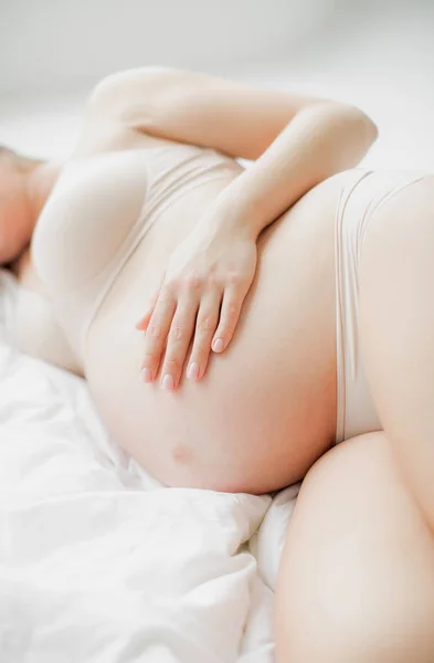 快乐的年轻母亲期待宝宝的出生 一个裸露的肚子的怀孕女孩躺在白床单上 — 图库照片