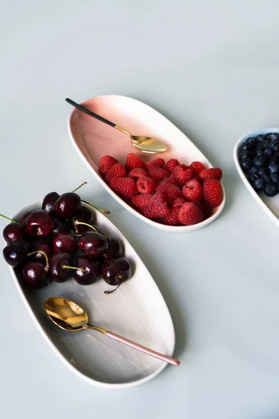 Yaz meyveleri yaban mersini, ahududu ve kiraz pembe, mavi ve gri renklerin yeni zarif tabaklar üzerinde. İzole beyaz arka plan üzerinde yukarıdan yeni lüks Altın çatal görünümü. Üstte görüntü.