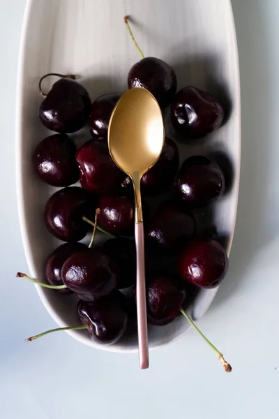 Pembe çay kaşığı ile gri renklerin yeni zarif tabaklar üzerinde Yaz meyveleri kiraz. İzole beyaz arka plan üzerinde yukarıdan yeni lüks Altın çatal görünümü. Üstte görüntü.