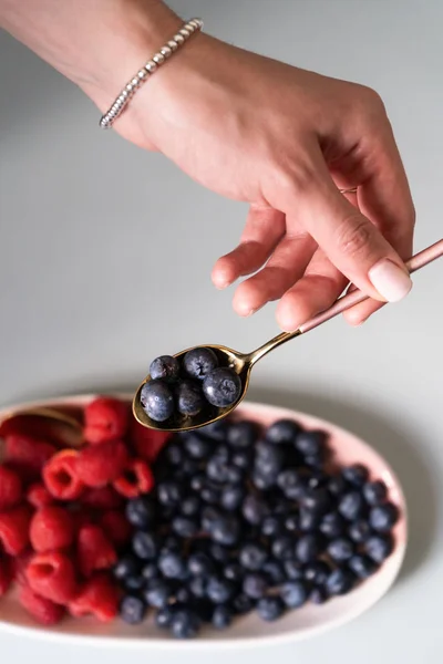 Yaz meyveleri yaban mersini, ahududu pembe renk yeni zarif tabaklar bir çay kaşığı tutan bir el ile. İzole beyaz arka plan üzerinde yukarıdan yeni lüks Altın çatal görünümü. Üstte görüntü.