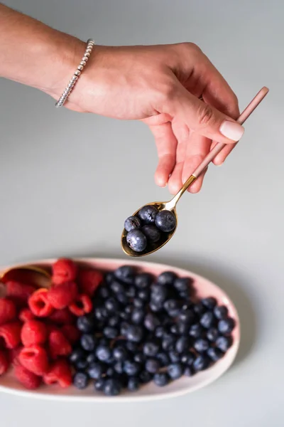 Yaz meyveleri yaban mersini, ahududu pembe renk yeni zarif tabaklar bir çay kaşığı tutan bir el ile. İzole beyaz arka plan üzerinde yukarıdan yeni lüks Altın çatal görünümü. Üstte görüntü.