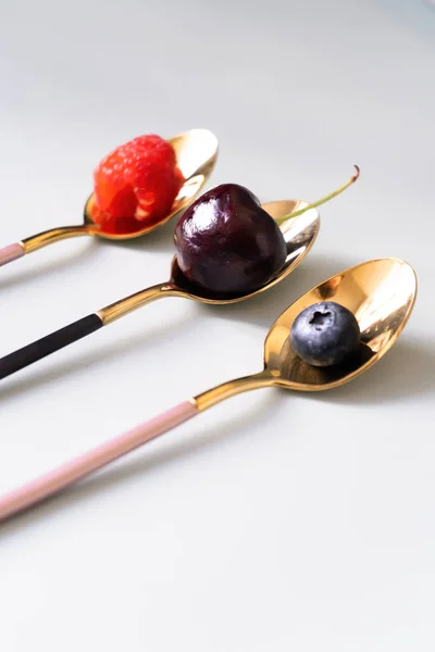 Siyah ve pembe renk çay kaşığı yaz meyveleri ahududu, yaban mersini ve kiraz vardır. İzole beyaz arka plan üzerinde yukarıdan yeni lüks Altın çatal görünümü. Üstte görüntü.