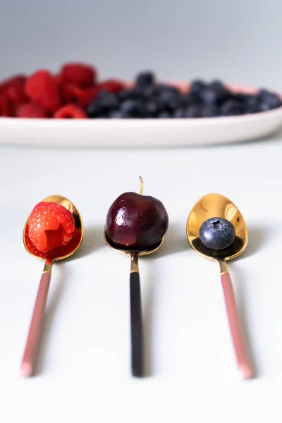 Yaz meyveleri yaban mersini, ahududu ve kiraz pembe, mavi ve gri renklerin yeni zarif tabaklar üzerinde. İzole beyaz arka plan üzerinde yukarıdan yeni lüks Altın çatal görünümü. Üstte görüntü.