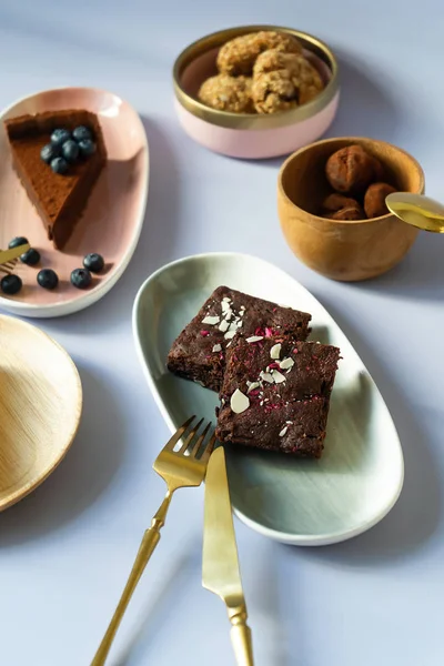 Farklı renklerde tabaklarda çilek ve fındık ile kek tatlılar Dilimleri, pembe, yeşil, ahşap malzeme. Yemek için bıçaklı Altın Çatal. Çay kaşığı. Çikolata, kek, cheesecake, bisküvi.